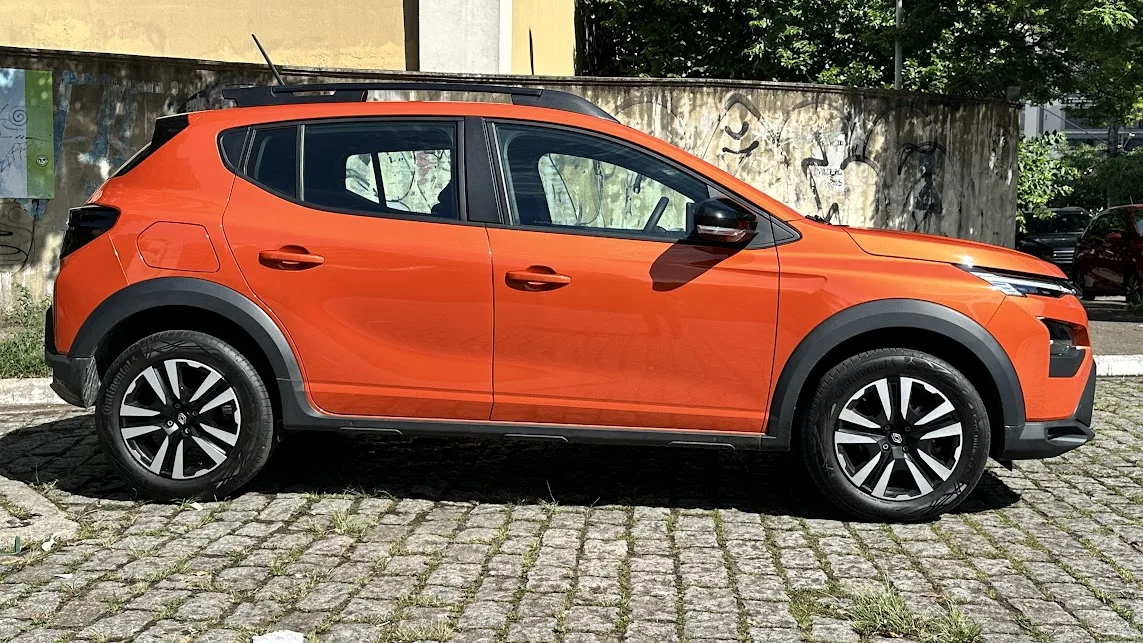 Renault Kardian manual laranja parado de lateral com árvore e muro ao fundo