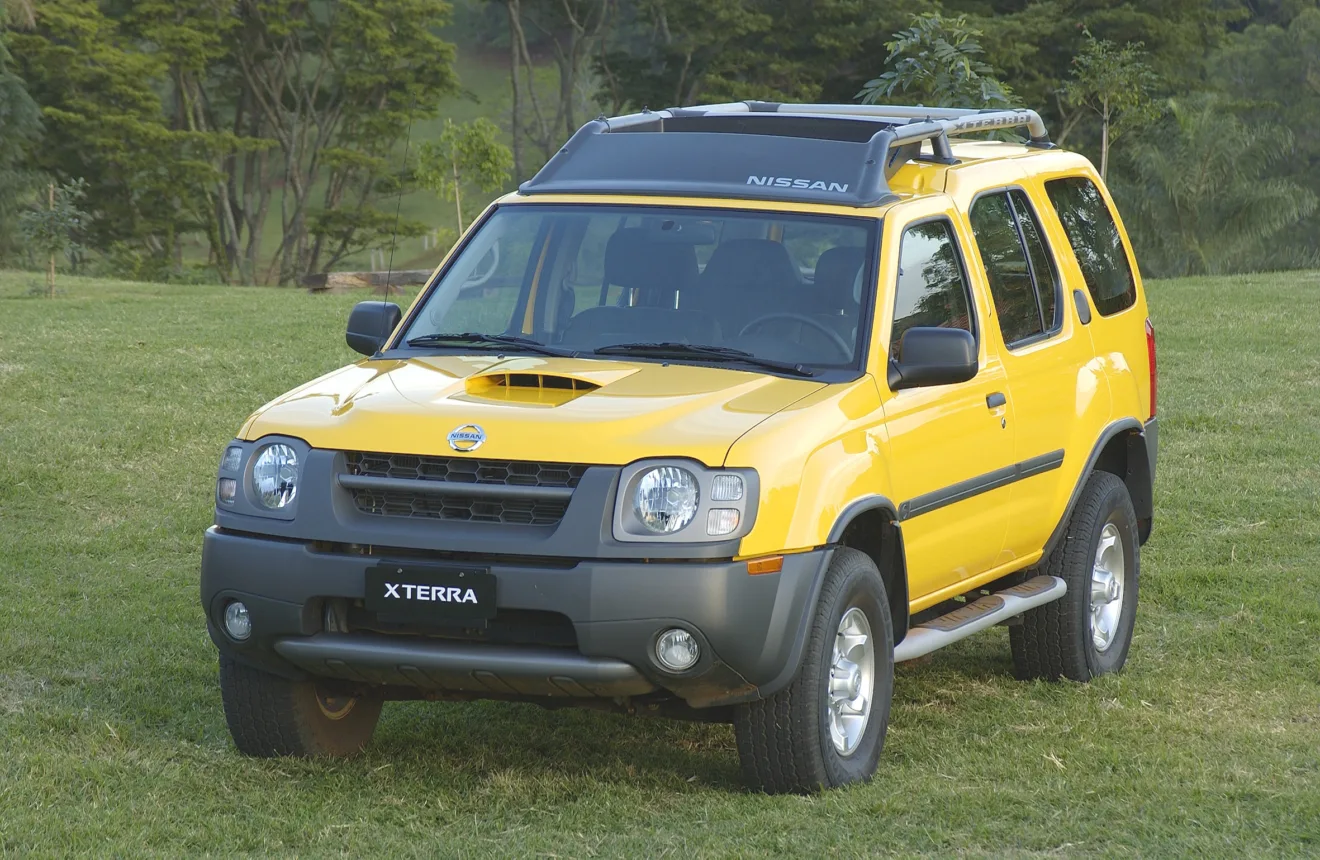 Nissan Xterra amarelo parado de frente na grama com árvores ao fundo