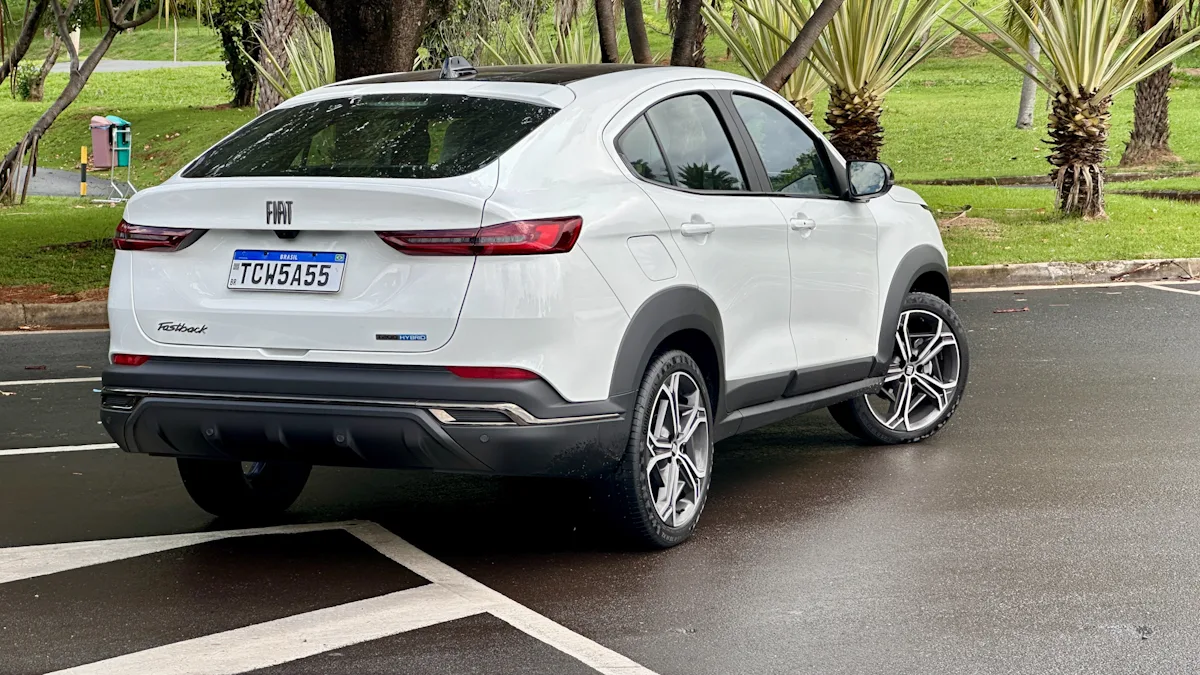 Fiat Fastback Hybrid branco de frente em um estacionamento molhado com uma floresta ao fundo