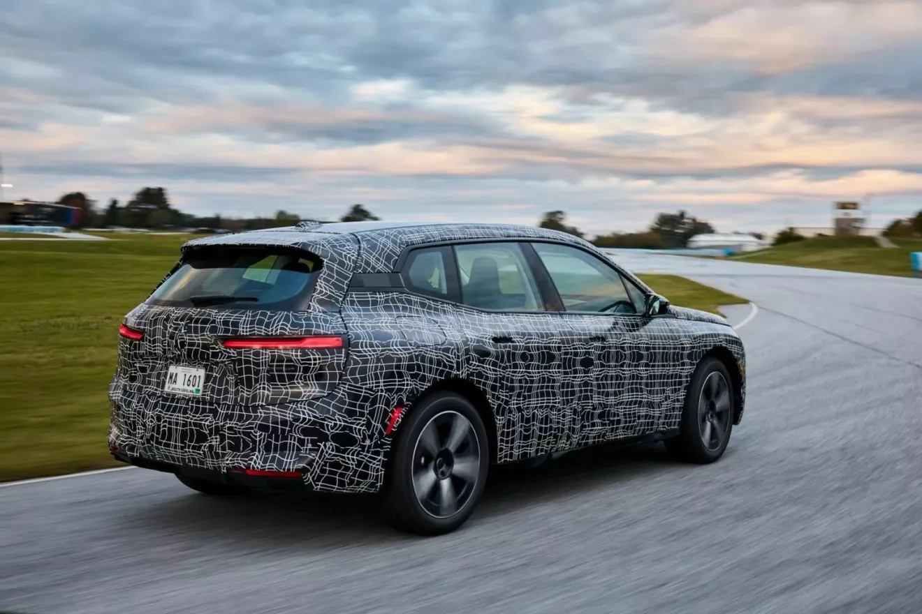 Novo BMW iX reestilizado camuflado de preto e branco, visto de trás e andando em uma pista