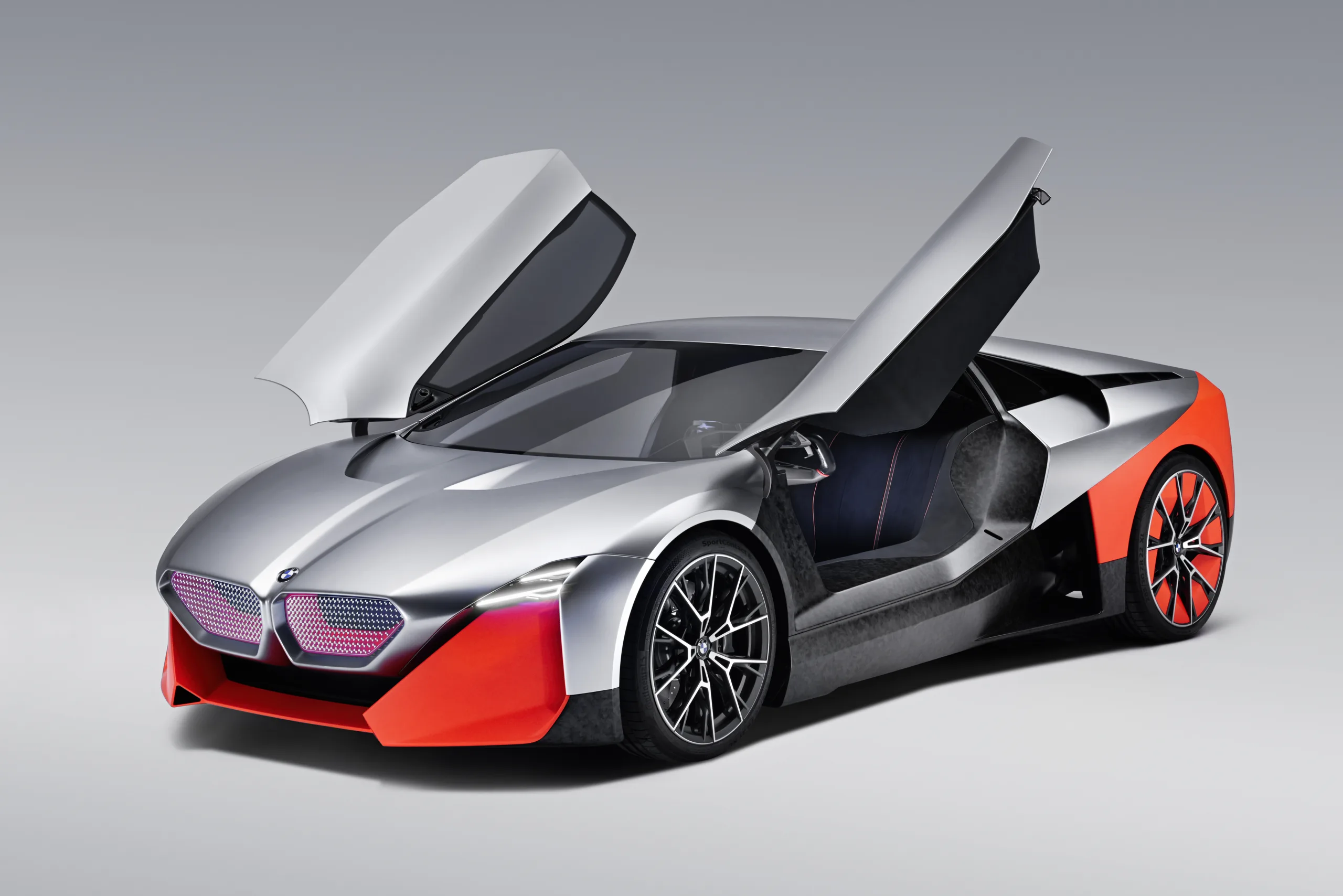 BMW Vision M Next prata com parte alaranjada, visto de frente, com portas abertas e fundo claro