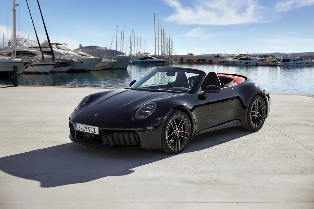 Porsche 911 Carrera GTS Cabriolet preto parado com a capota aberta com mar e barcos ao fundo