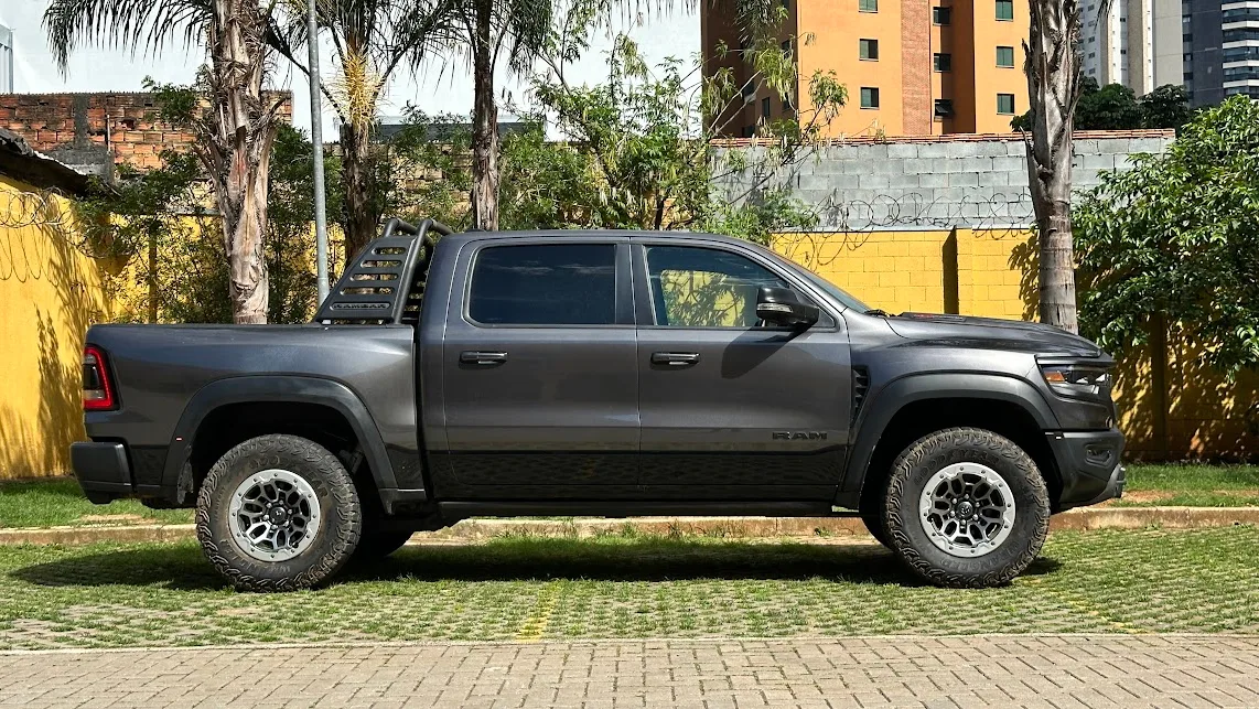 Ram 1500 TRX cinza parada de lateral com árvore e muro amarelo ao fundo