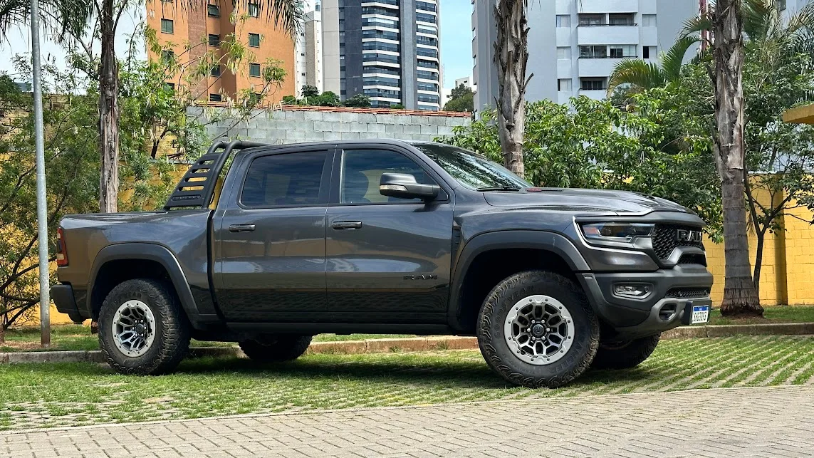 Ram 1500 TRX cinza de lateral com as rodas dianteiras viradas e árvores ao fundo