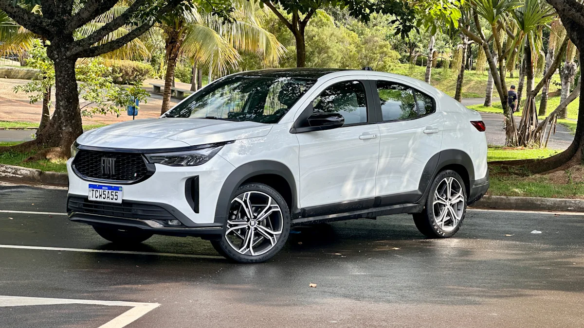 Fiat Fastback Hybrid branco de frente em um estacionamento molhado com uma floresta ao fundo