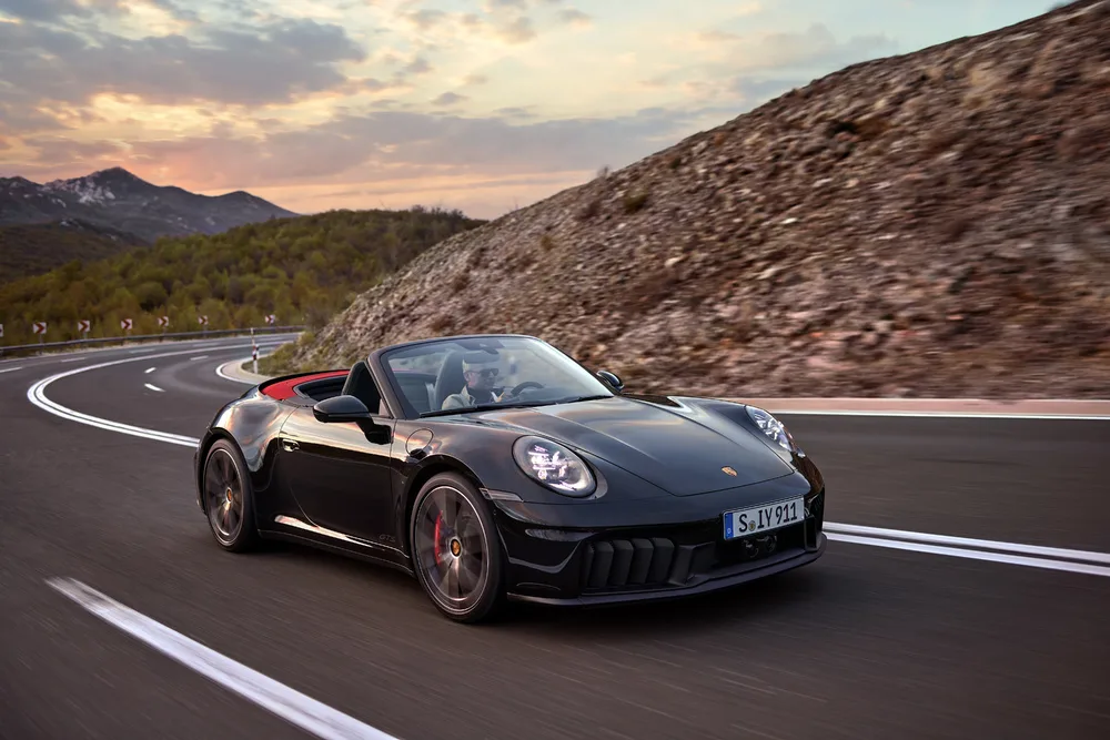 Porsche 911 Carrera GTS Cabriolet preto com a capota aberta andando na estrada com montanhas ao fundo