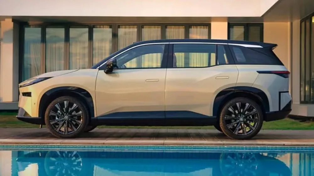 Vista lateral do Toyota bZ3X creme com teto preto, piscina e casa ao lado