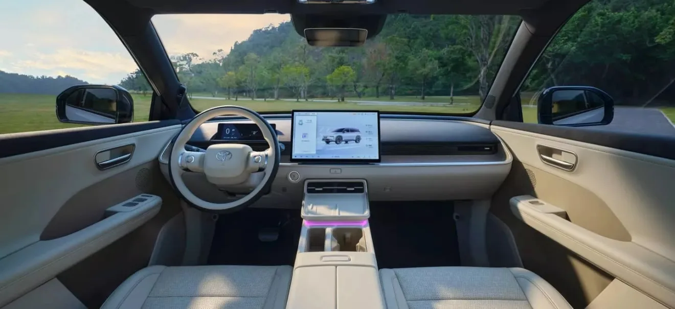 Interior do Toyota bZ3X com painel de instrumentos e central multimídia ligados e mato ao fundo
