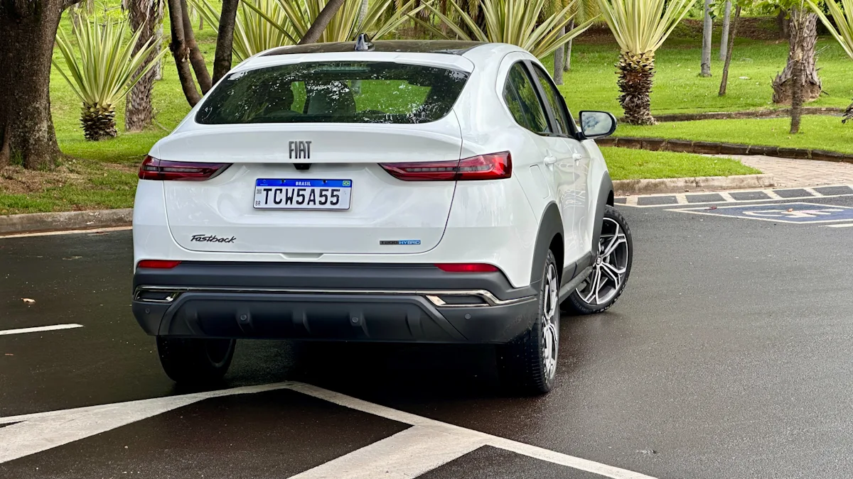 Fiat Fastback Hybrid branco de traseira em um estacionamento molhado com uma floresta ao fundo