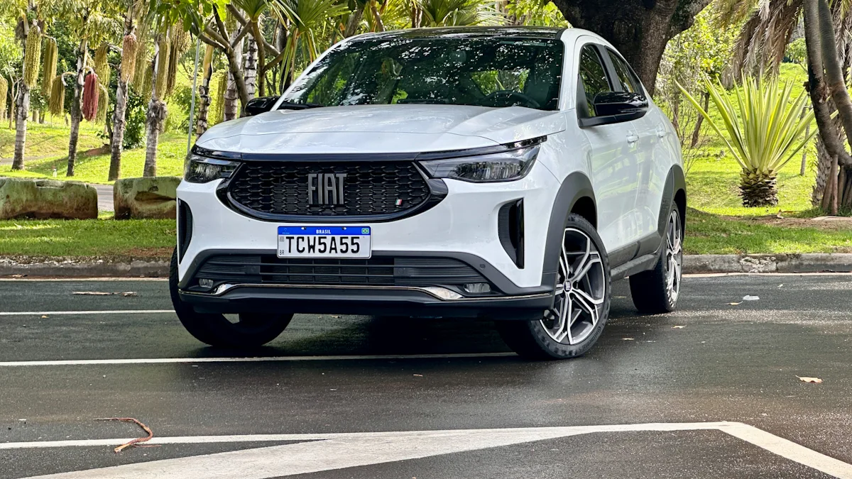 Fiat Fastback Hybrid branco de frente em um estacionamento molhado com uma floresta ao fundo