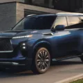 Infiniti QX80 azul, visto de frente, parado, com faróis acesos e casa ao fundo