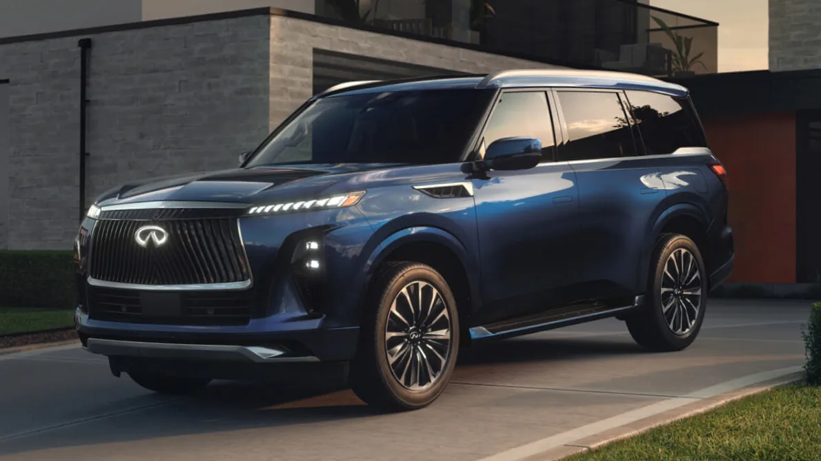 Infiniti QX80 azul, visto de frente, parado, com faróis acesos e casa ao fundo