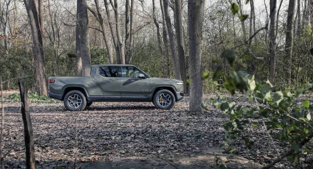 Rivian R1T cinza parada de lateral na floresta