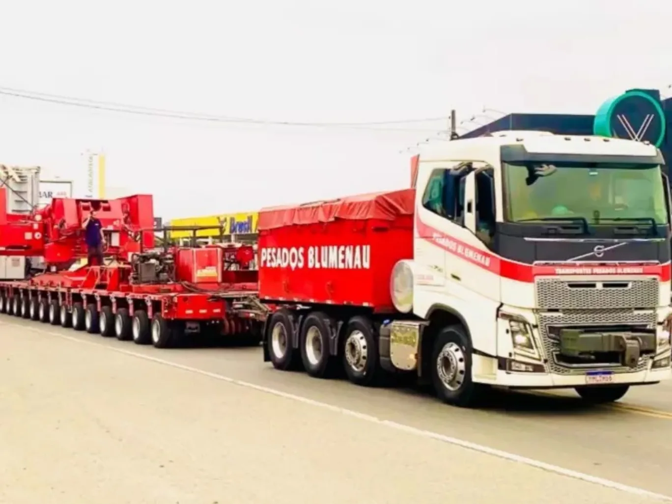 Caminhão branco com caçamba e partes vermelhas levando carga e visto de frente