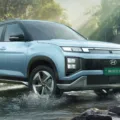 Hyundai Creta elétrico azul, com faróis acesos, visto de frente e andando na água