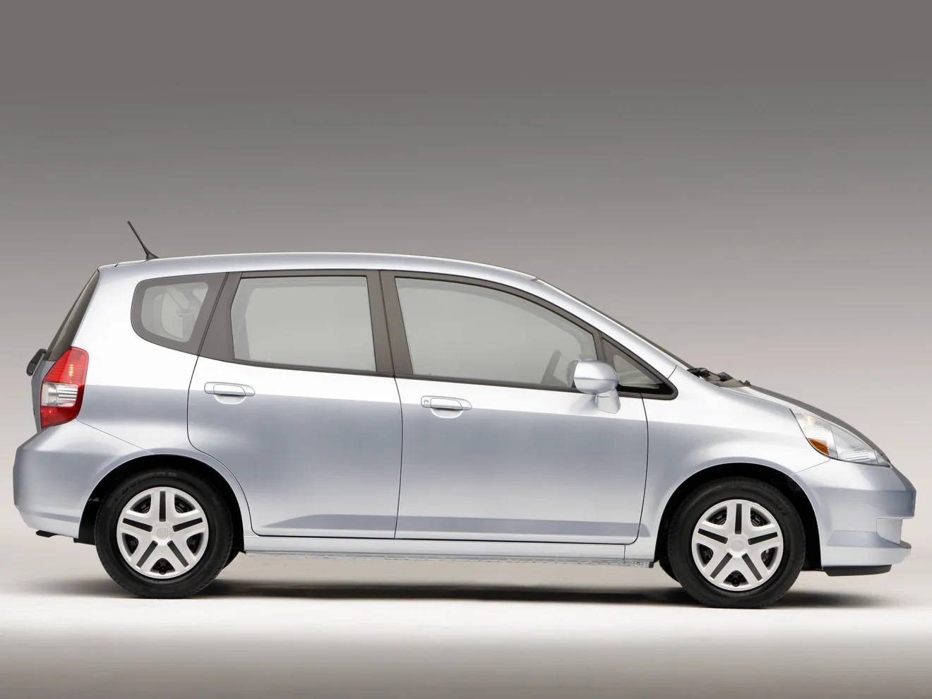 Honda Fit de primeira geração prata de lado com fundo neutro