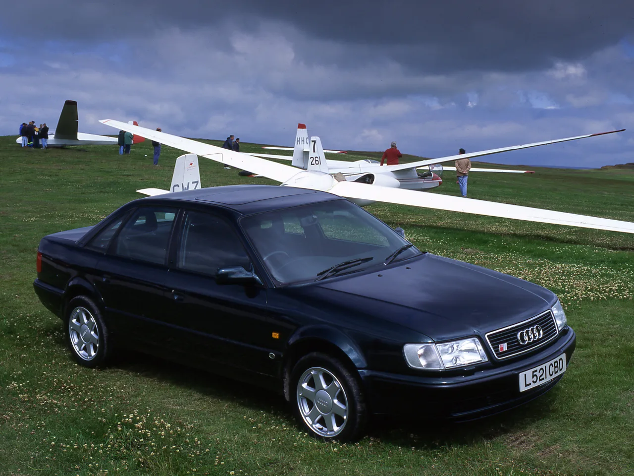 Audi 100 S4 preto estacionado sobre a grama com planadores ao fundo 