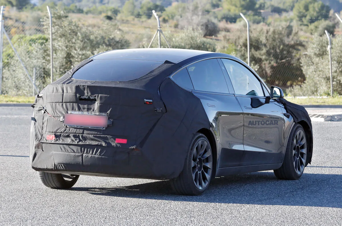 Tesla Model Y reestilizado camuflado de preto, visto lateralmente e com mato ao fundo