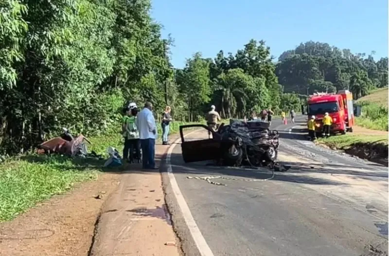 Carro destruído logo após acidente na SC-157, com mato ao redor e caminhão dos bombeiros ao fundo