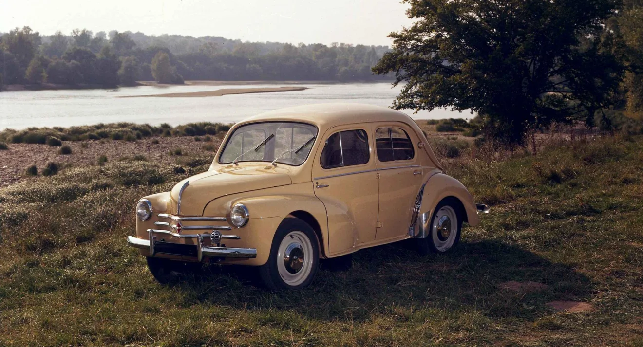 Renault 4CV bege parado de frente e lateral com lago ao fundo