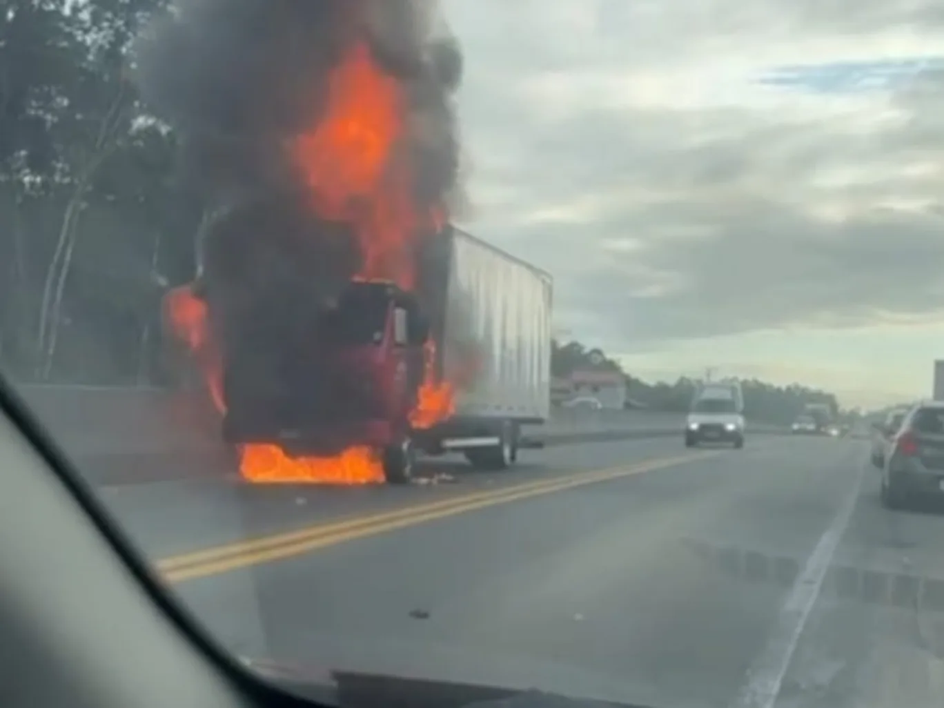 Caminhão que pegou fogo na BR-470 com fumaça escura e carro ao redor