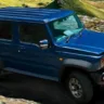 Suzuki Jimny Nomade azul, visto de lado e andando em estrada de terra