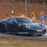 Porsche 718 Cayman elétrico camuflado de preto, visto lateralmente com placas ao lado e faróis acesos