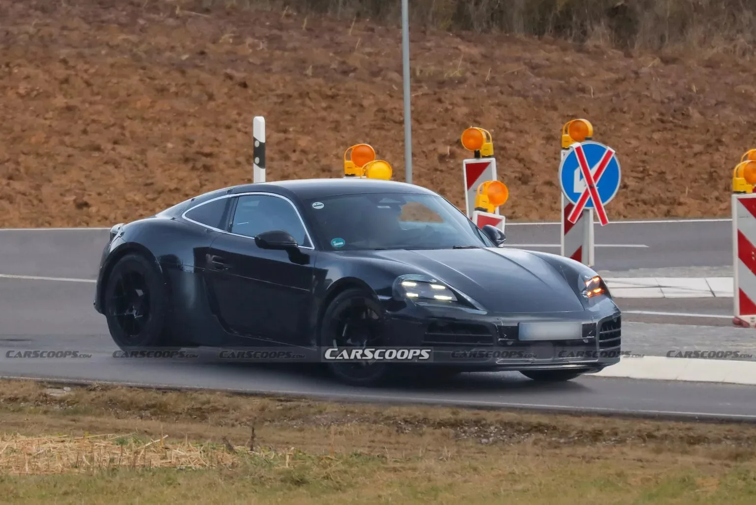 Porsche 718 Cayman elétrico camuflado de preto, visto lateralmente com placas ao lado e faróis acesos