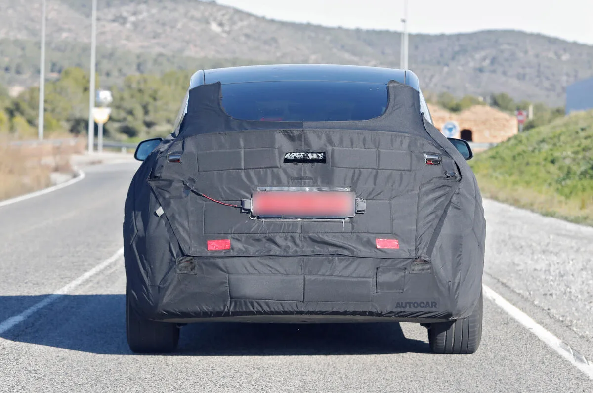 Tesla Model Y reestilizado camuflado de preto, visto de trás e com rodovia ao fundo