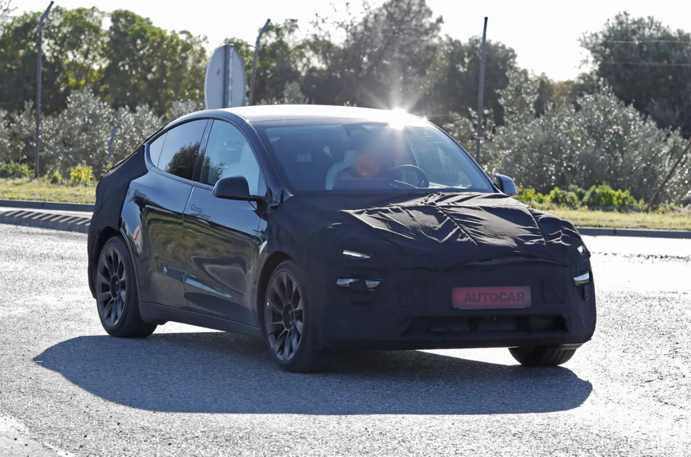 Tesla Model Y reestilizado camuflado de preto, visto de frente e com mato ao fundo