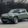 Rivian R1T cinza andando na estrada com árvores ao fundo