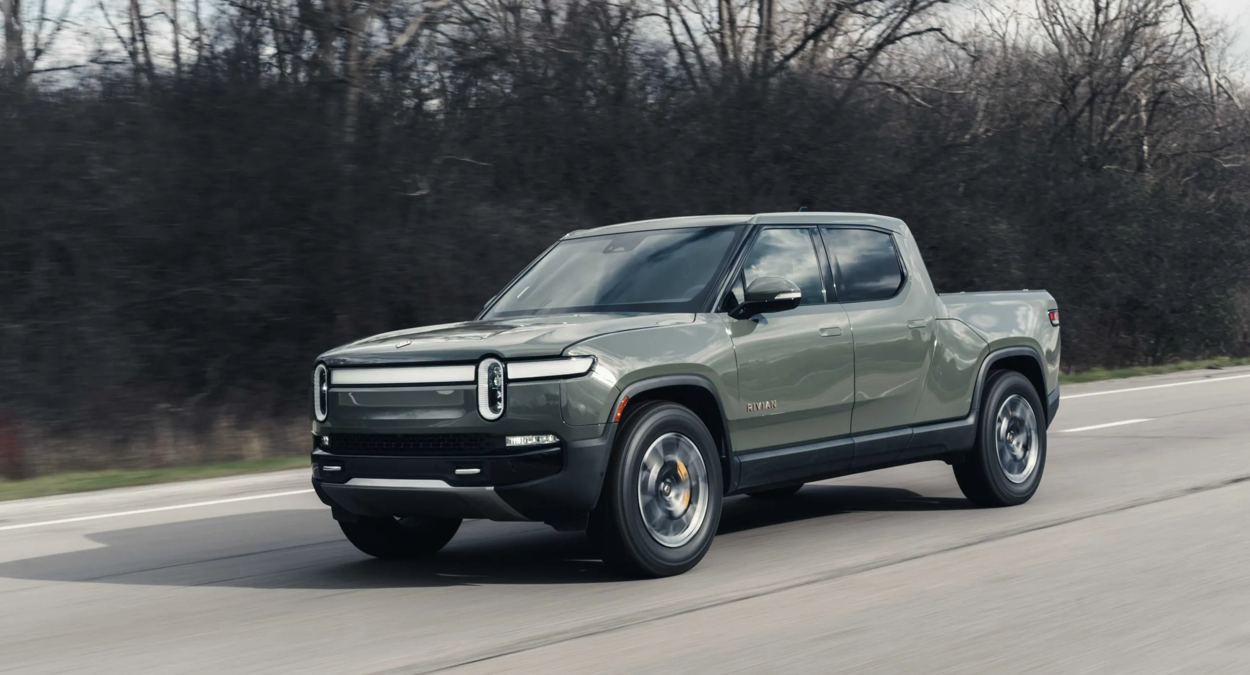 Rivian R1T cinza andando na estrada com árvores ao fundo