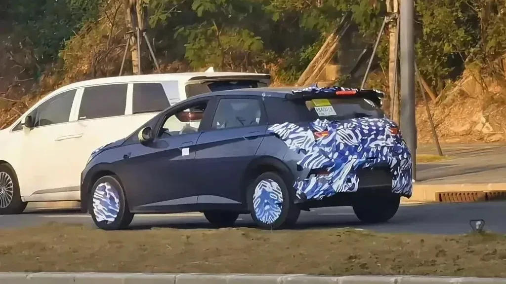 BYD Dolphin reestilizado azul, camuflado de azul e branco, visto de trás e com carro branco ao fundo