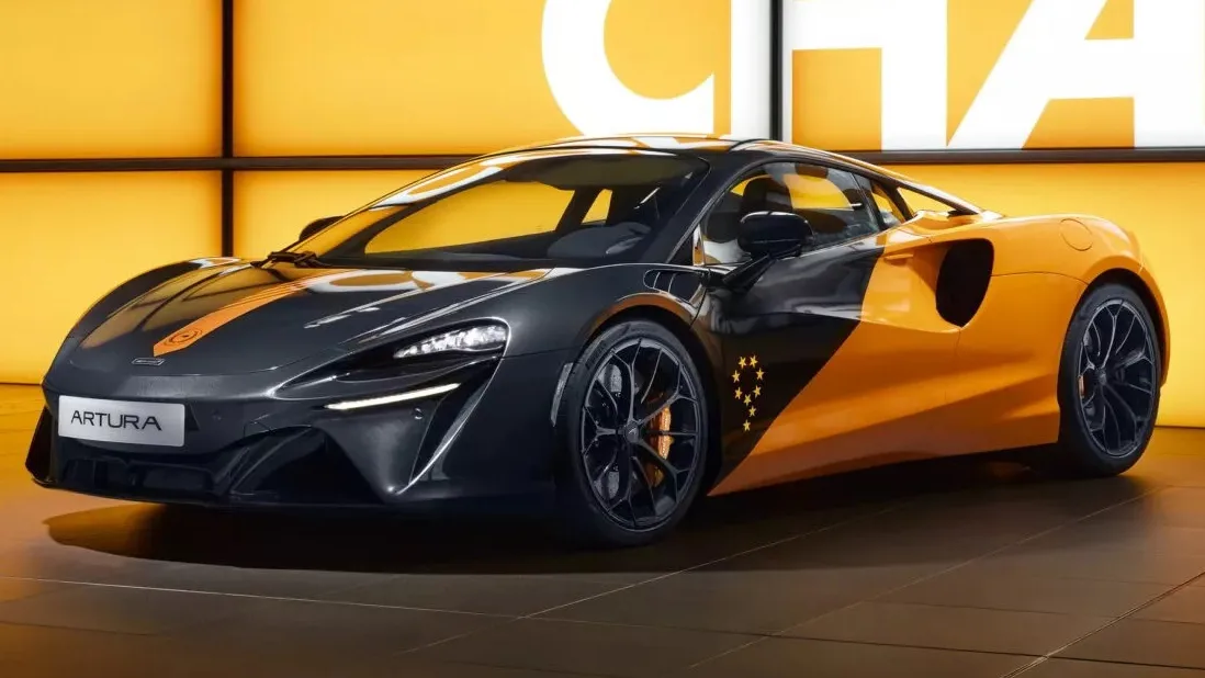 McLaren Artura MCL38 preto e laranja, visto de frente e com letreiro ao fundo