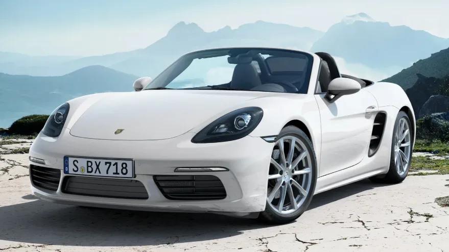 Porsche 718 Boxster branco, visto de frente, com teto aberto e montanhas ao fundo