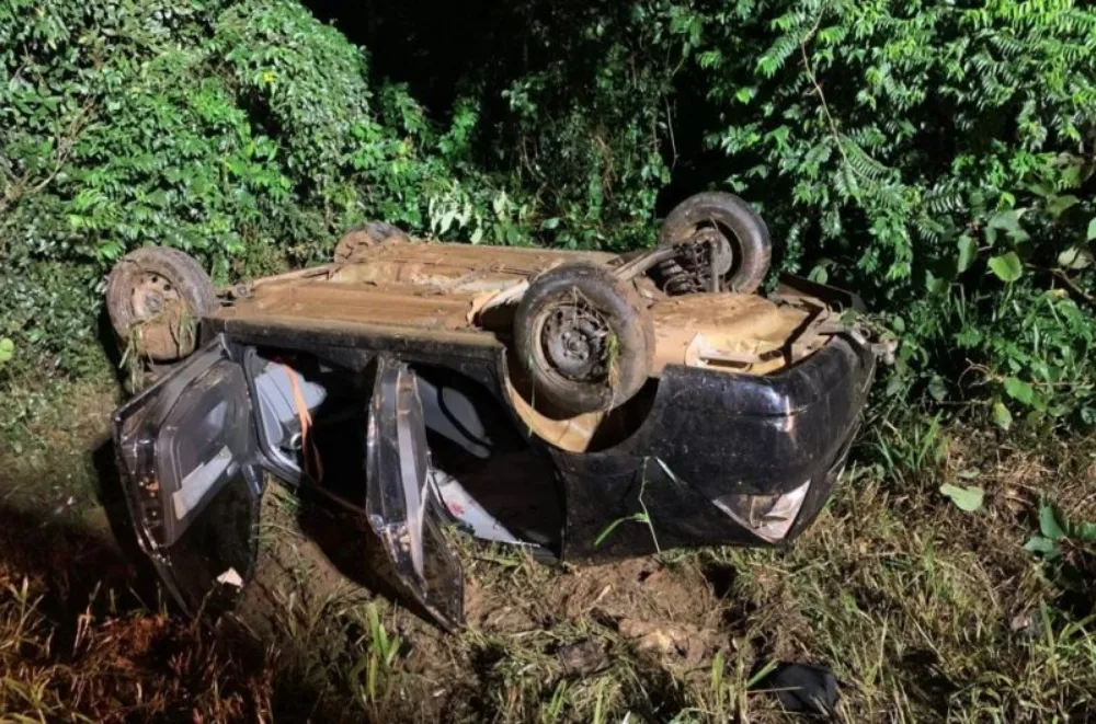 Ford Fiesta sedan preto capotado após acidente com mato ao redor