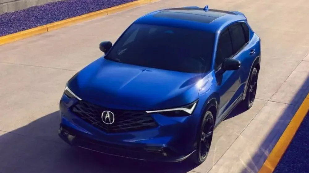 Acura ADX azul, visto de frente, parado, com detalhes pretos e faróis acesos