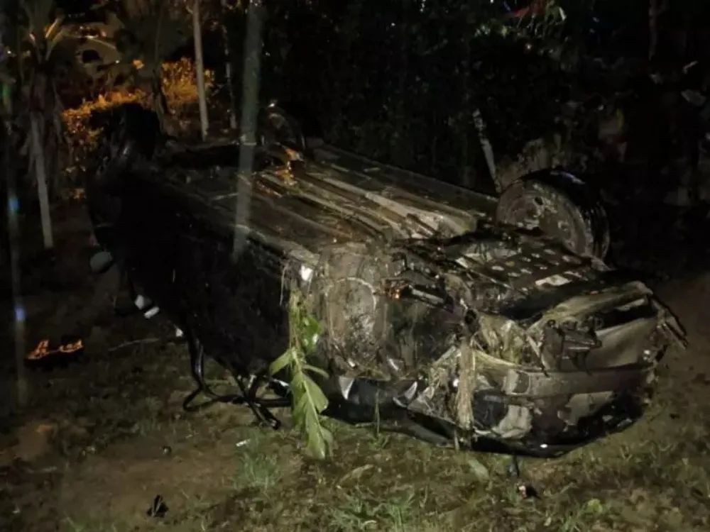 Carro escuro capotado no mato e destruído após acidente na BR-470