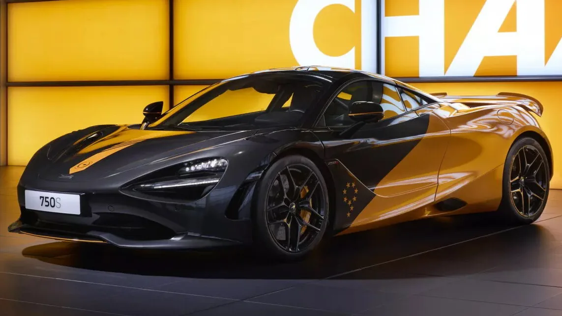 McLaren 750S MCL38 preto e laranja, visto de frente e com letreiro ao fundo