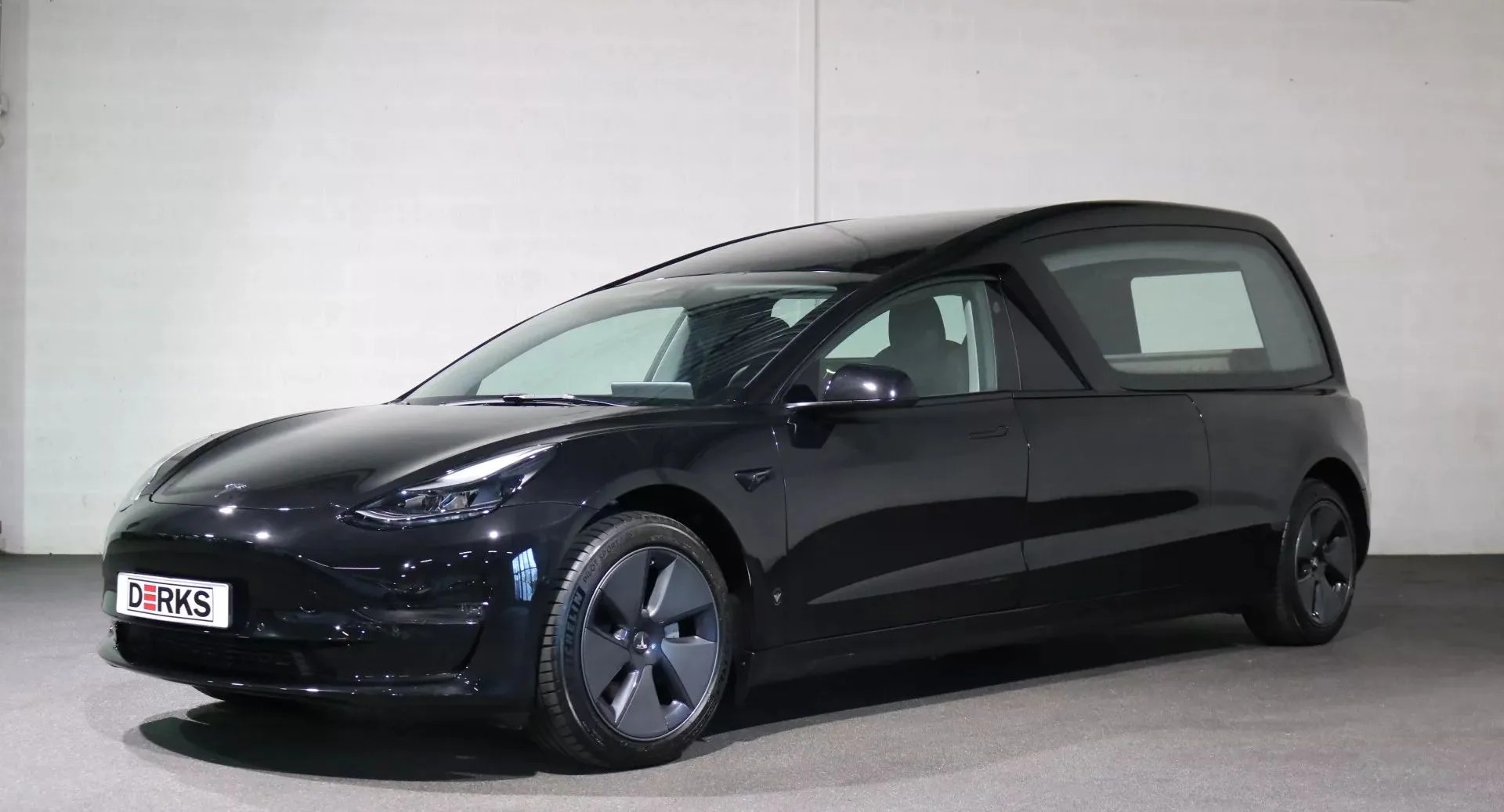 Tesla Model 3 preto fúnebre para de frente com parede branca ao fundo