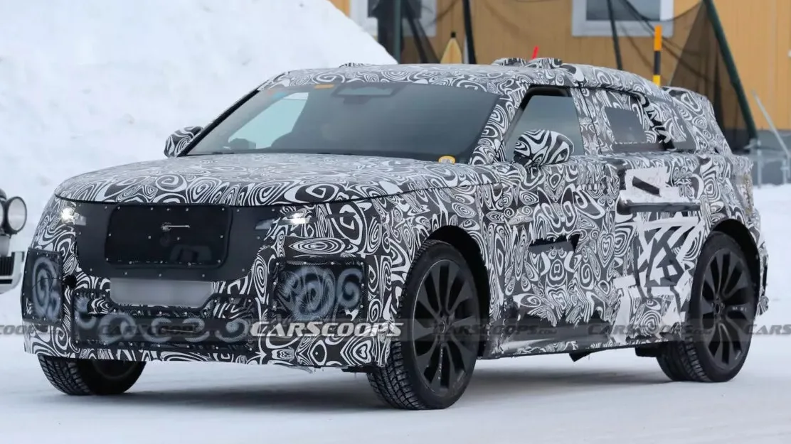 Protótipo do Land Rover Range Rover Velar elétrico camuflado de preto e branco, visto de frente, com faróis acesos e neve ao fundo