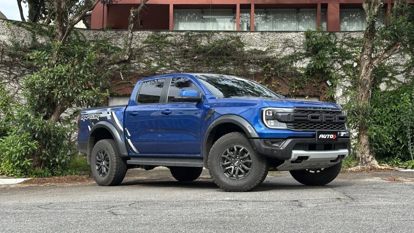 Ford Ranger Raptor azul parada de frente e lateral com portão branco ao fundo