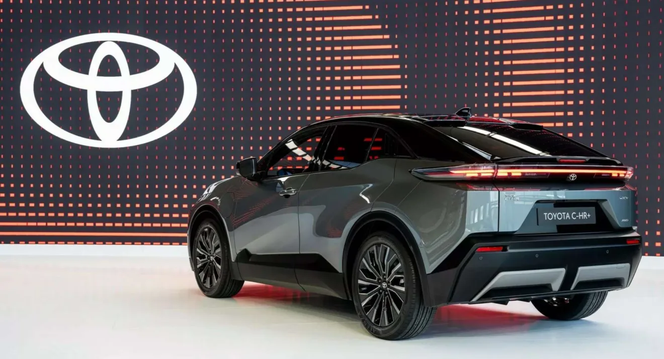 Toyota C-HR+ verde parado de traseira com logotipo do fabricante ao fundo