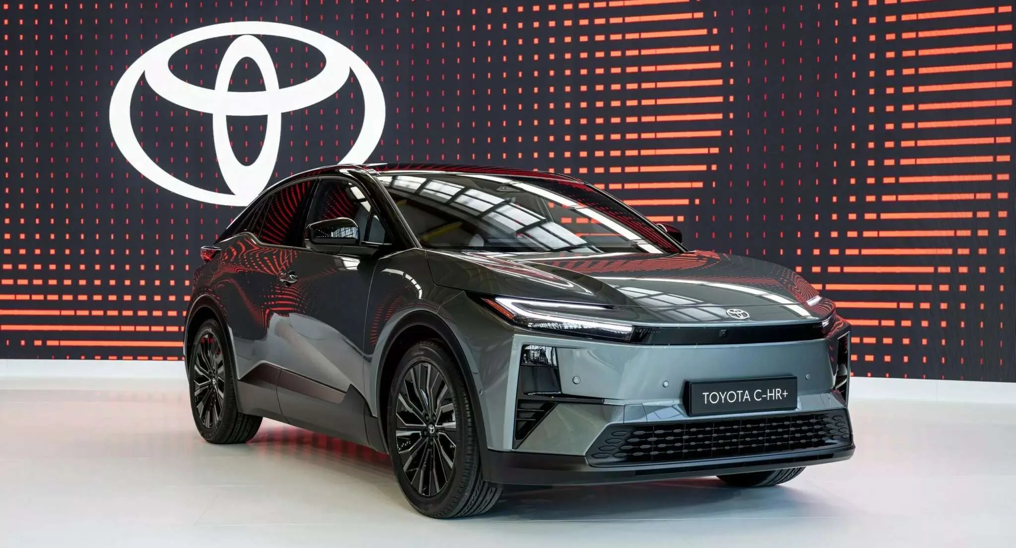 Toyota C-HR+ verde parado de frente com logotipo do fabricante ao fundo