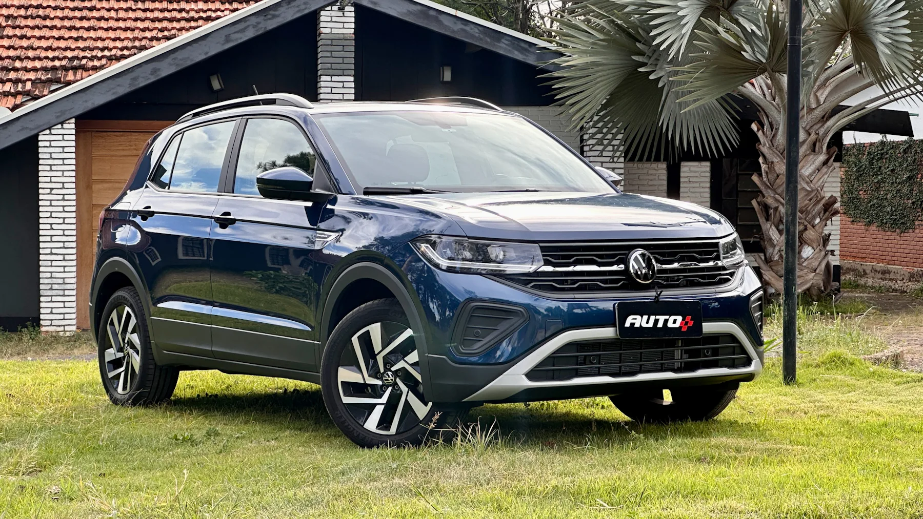 Volkswagen T-Cross Comfortline azul de frente em um gramado com uma casa ao fundo