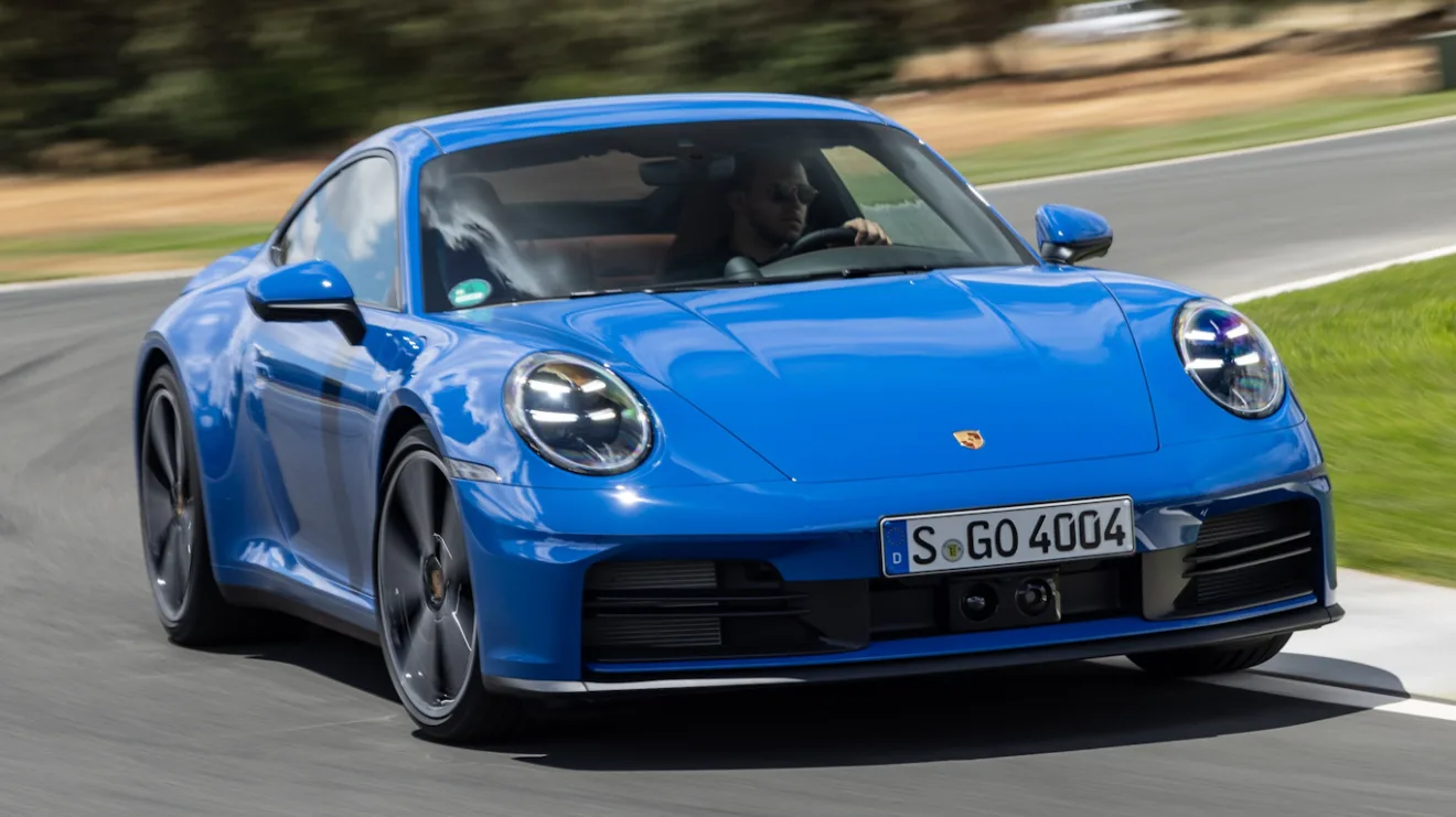 Novo Porsche 911 Carrera Coupé azul, visto de frente, com faróis acesos e andando em pista