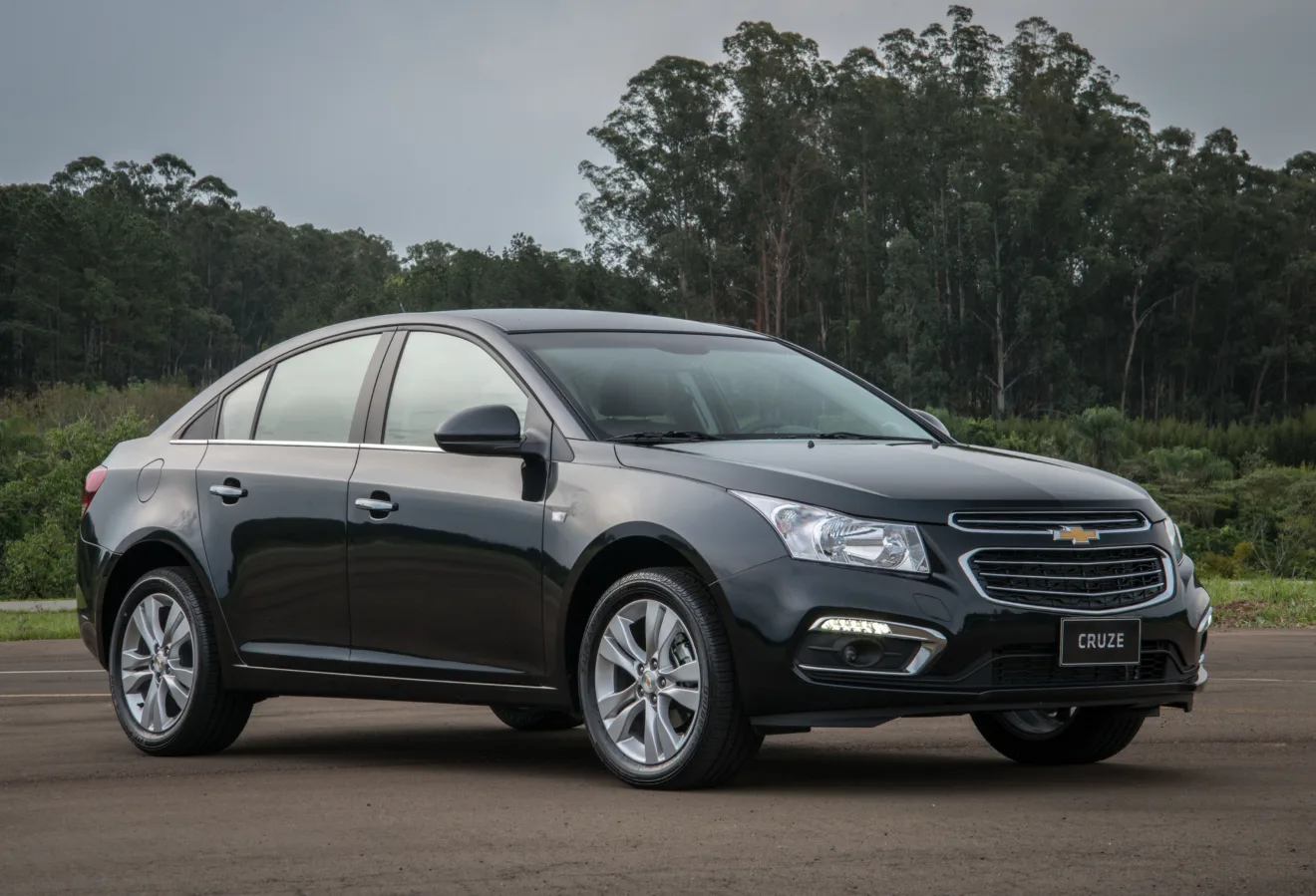 Chevrolet Cruze Sedan preto, visto de frente, com mato ao fundo e DRL's acesos