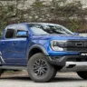 Ford Ranger Raptor azul parada de frente com portão branco ao fundo