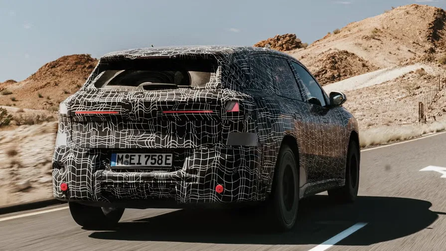 Protótipo camuflado de preto do novo BMW iX3 da linha Neue Klasse, visto de trás e com lanternas acesas