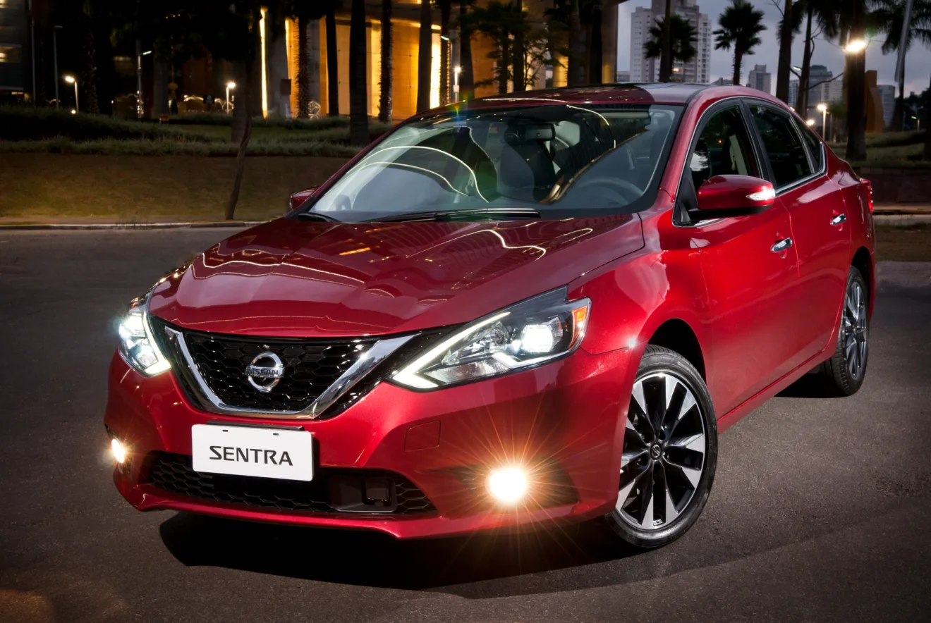 Nissan Sentra vermelho, visto de frente e com faróis acesos